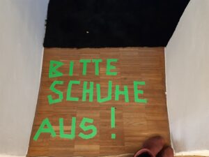 Schrift auf Boden aus Klebestreifen: "Bitte Schuhe aus"