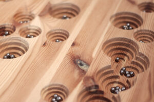 Kleine Murmeln, die auf einer Holzplatte in Einfräsungen liegen 