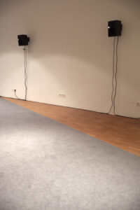 Am Boden Teppich ausgelegt, an der Wand sind Lautsprecher angebracht 